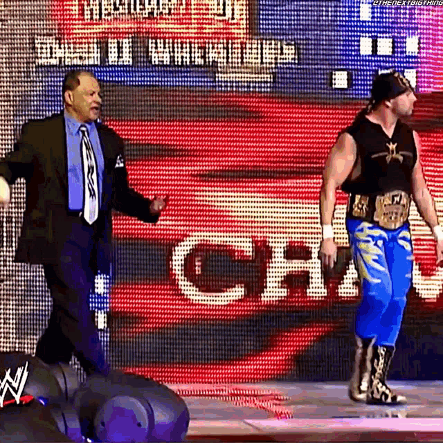 a man in a suit and tie stands next to a wrestler in blue pants .