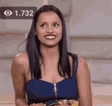 a woman in a blue top is smiling and looking at the camera while holding a cell phone .