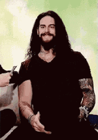 a man with long hair and a beard is wearing a black shirt and a tattoo on his arm .