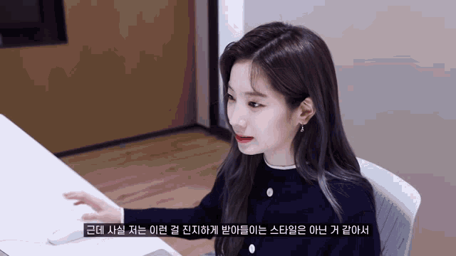 a woman sitting at a desk with korean writing on the bottom of the screen