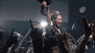 a woman is holding a drum in her hand while a crowd applauds