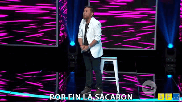 a man in a white jacket stands on a stage with the words por fin la sacaron written below him