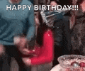 a group of people are standing around a birthday cake and a man is holding a red object .