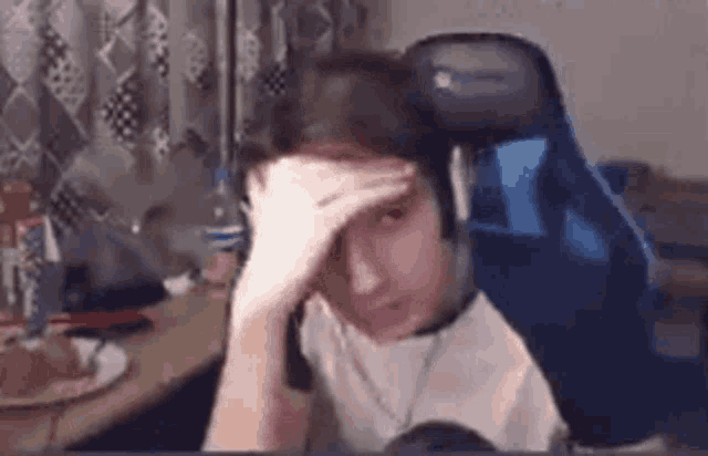 a person is sitting in a gaming chair with headphones on and covering their face with their hand .