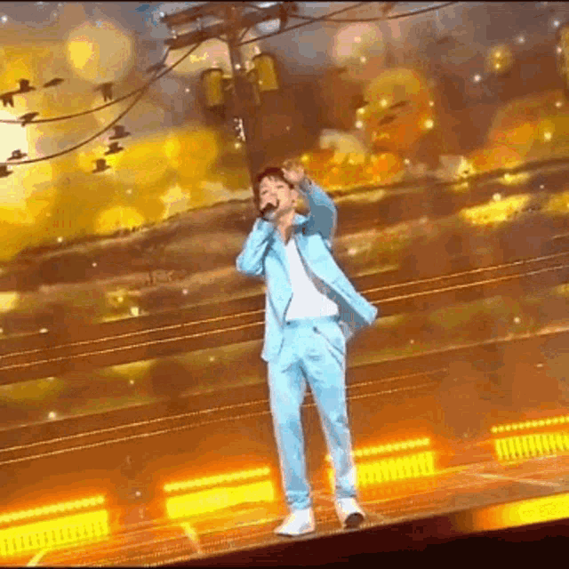 a man in a blue suit is singing into a microphone on stage .