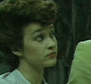 a close up of a woman 's face with a man in a green jacket behind her .