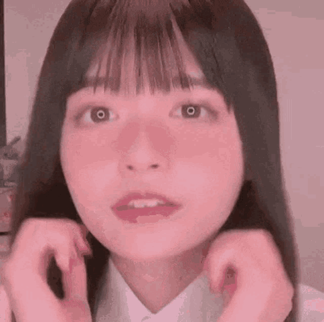 a close up of a girl 's face with her hands on her face and a pink background .