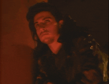 a man with long hair and a beard is wearing a leather jacket and looking up .