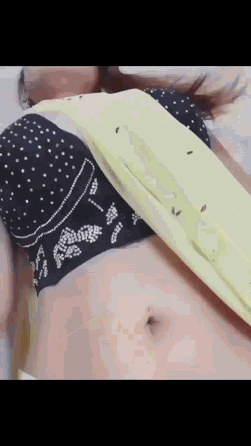 a woman wearing a black bra and a yellow saree is laying on a bed .
