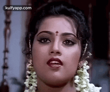 a close up of a woman 's face with a flower garland around her neck and earrings .