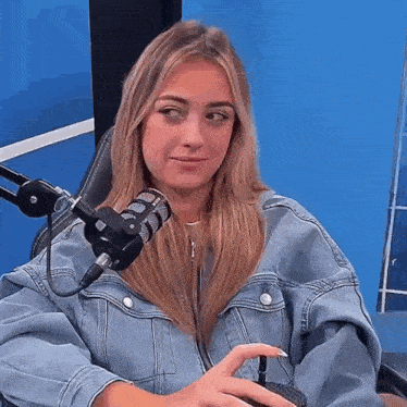 a woman in a denim jacket is sitting in front of a microphone in a studio .