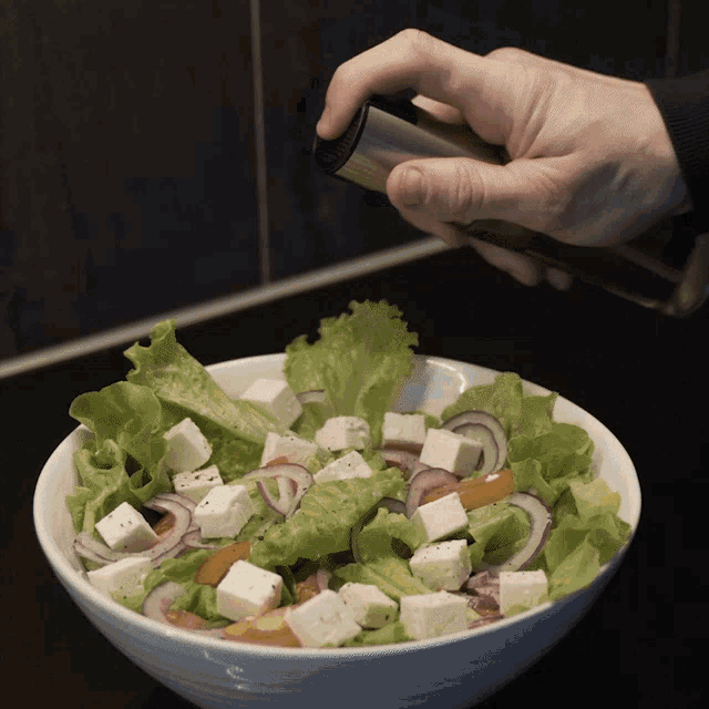 a person is sprinkling olive oil on a salad in a bowl