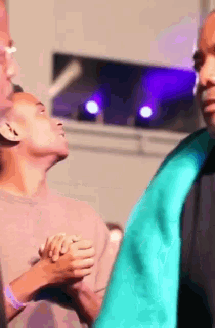 a man in a green robe holds hands with another man in a pink shirt