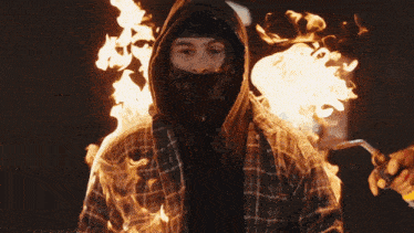 a man in a plaid shirt with a hood on is surrounded by flames