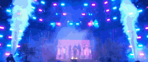a group of people are dancing on a stage with smoke coming out of the smoke stacks