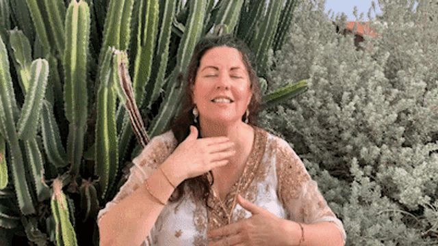 a woman is standing in front of a cactus plant with her eyes closed .