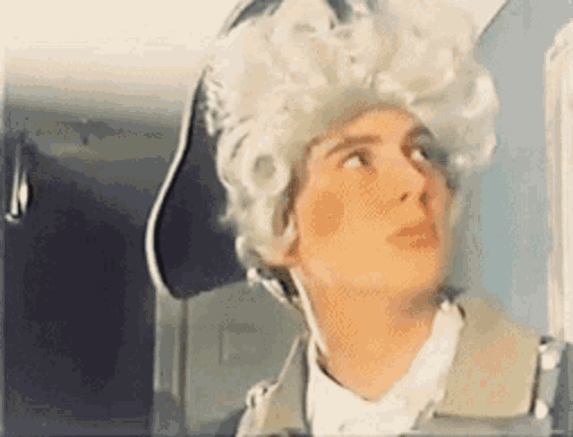 a man wearing a white wig and a hat is looking out a window .