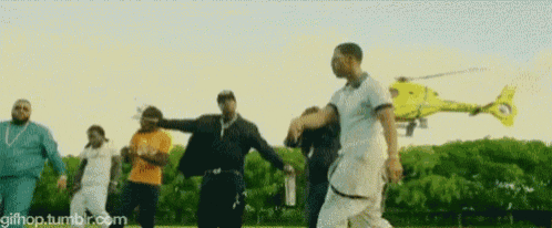 a group of men are dancing in front of a helicopter in a park .