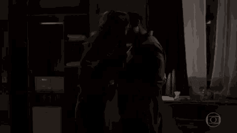 a couple is kissing in a dark room in front of a window .