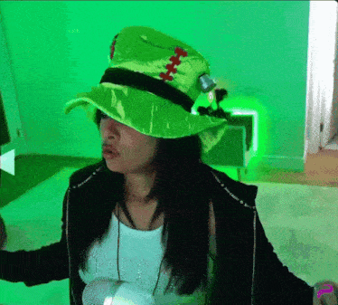 a woman wearing a green hat and a black jacket stands in front of a green screen