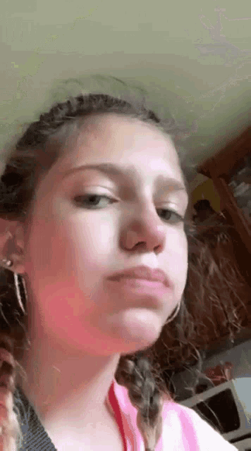 a young girl is making a funny face while wearing earrings and a pink shirt .