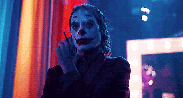 the joker is smoking a cigarette and talking on a cell phone in a dark room .