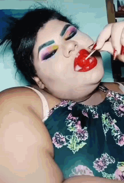 a woman in a floral top is eating a lollipop
