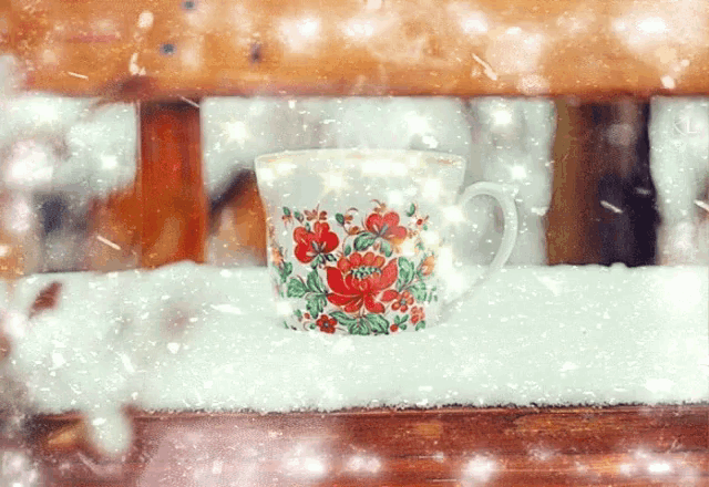a cup with flowers on it sits on a snowy bench