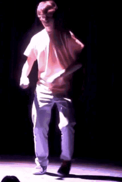 a man in an orange shirt and white pants is dancing on stage