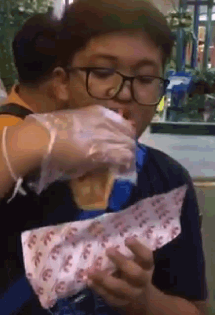 a boy wearing glasses is eating a piece of food with a wrapper that says ' ice ' on it