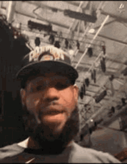 a man with a beard is wearing a hat and taking a selfie in a gym .