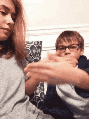 a boy and a girl are sitting on a couch playing with their hands