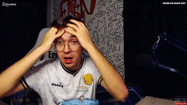 a man wearing glasses and a diadora shirt is sitting in front of a microphone .