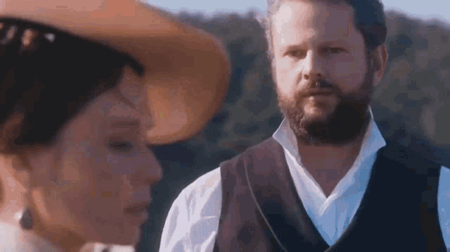 a man with a beard and a woman with a hat are looking at each other .