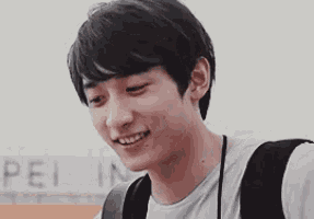 a young man with a backpack is smiling and looking down .