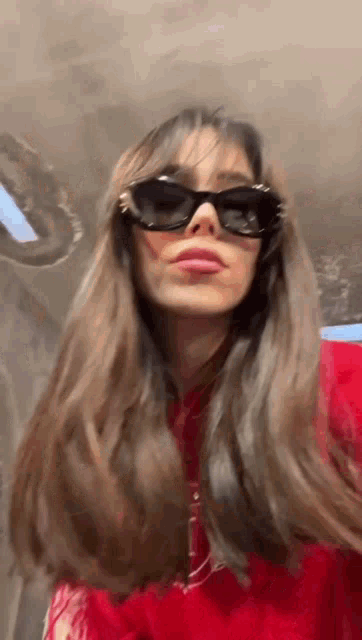 a woman wearing sunglasses and a red sweater is looking at the camera .