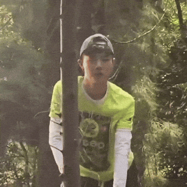a man in a neon yellow shirt is standing next to a tree in the woods