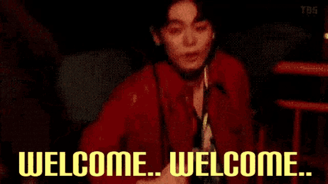 a man in a red jacket is sitting in a dark room with the words `` welcome welcome '' written on the screen .