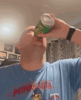 a man wearing a minnesota shirt is drinking from a green can