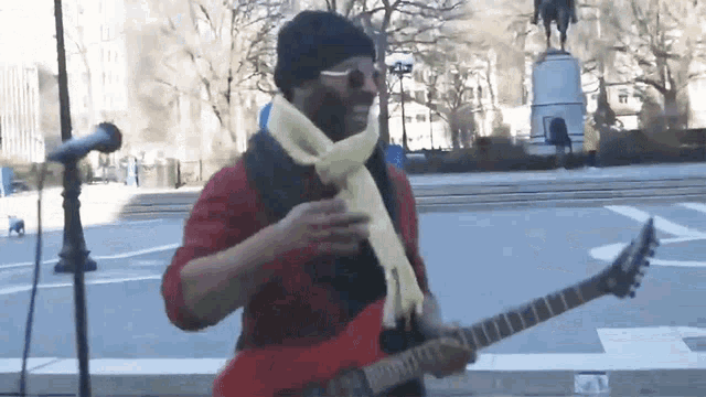 a man in a red shirt and yellow scarf is playing a guitar