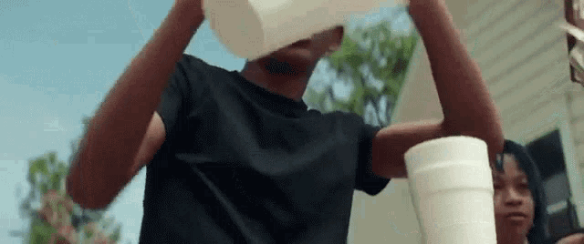 a man in a black shirt is holding a styrofoam cup in his hands .