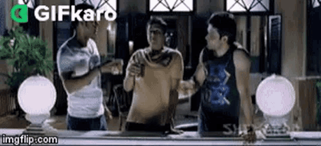 three men are standing around a table talking to each other .