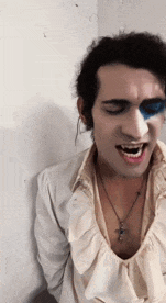 a man with blue paint on his face is wearing a white shirt and a cross necklace .