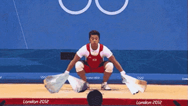 a man squatting down on a wrestling mat at the london 2012 olympic games