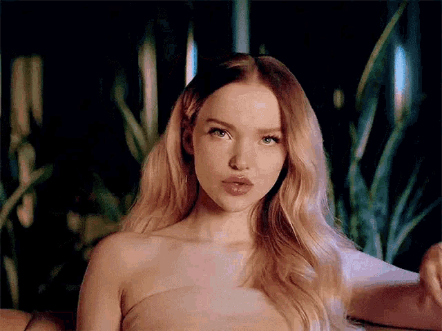 a woman with long blonde hair is wearing a strapless dress and making a funny face .