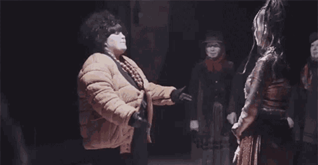 a woman in a brown jacket is standing in a dark room holding hands with two other women .