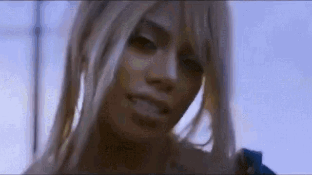 a close up of a woman 's face with long blonde hair and a blue sky in the background .