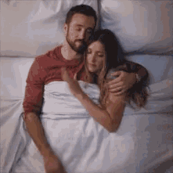 a man and a woman are hugging in bed .