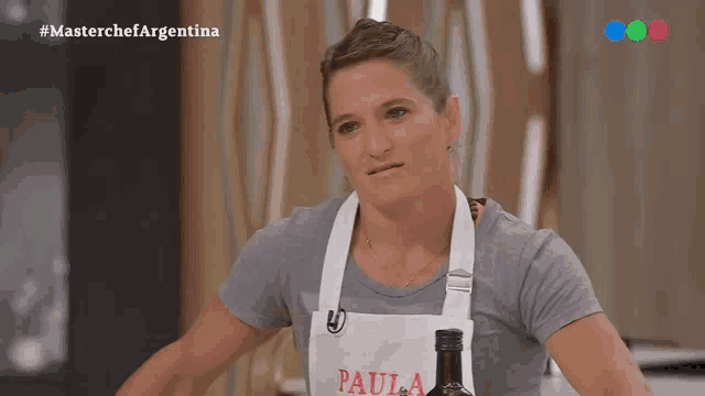 a woman wearing an apron that says paula holds a bottle