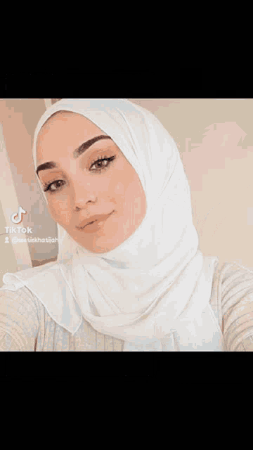 a woman wearing a white hijab is taking a picture of herself .